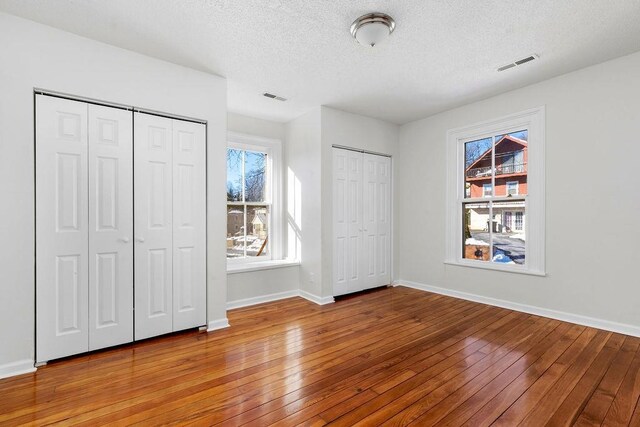 unfurnished bedroom with hardwood / wood-style flooring, a textured ceiling, and two closets