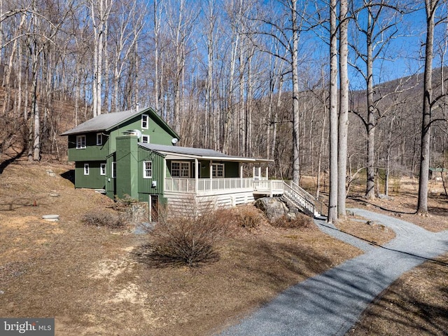 view of front facade with a porch, stairway, and a view of trees