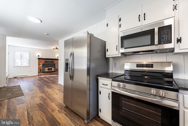 kitchen with appliances with stainless steel finishes, a brick fireplace, dark wood finished floors, and white cabinets