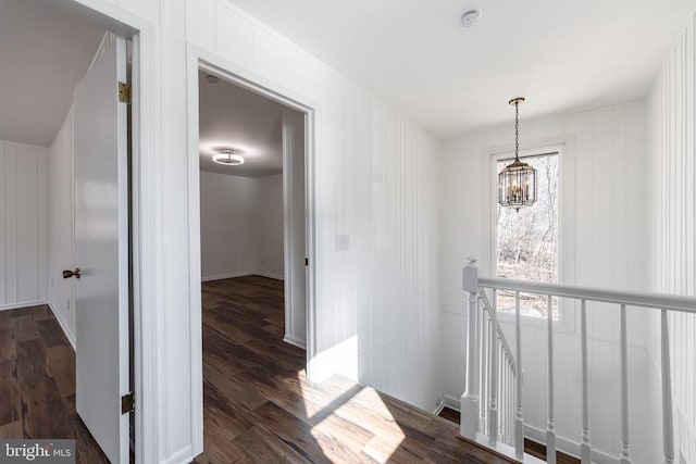 corridor featuring an inviting chandelier, dark wood finished floors, and an upstairs landing