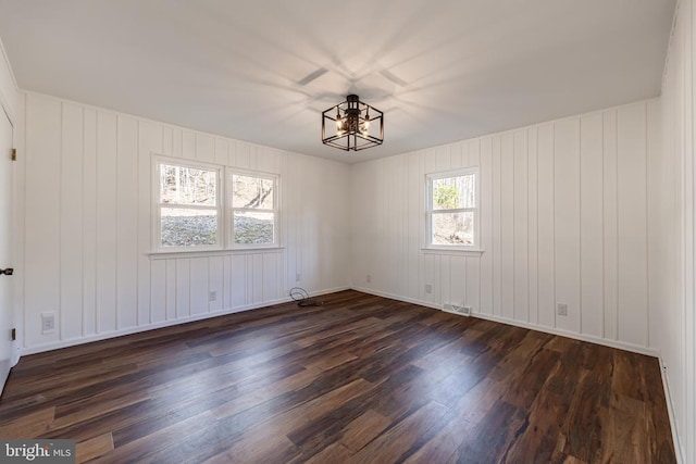 unfurnished room with an inviting chandelier, visible vents, and dark wood finished floors