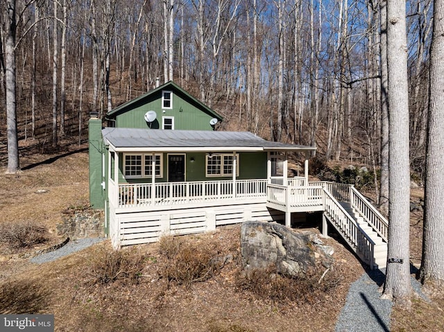 chalet / cabin featuring covered porch, a view of trees, and stairs