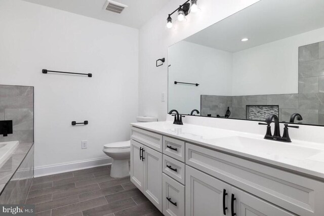 bathroom featuring vanity, tiled bath, and toilet