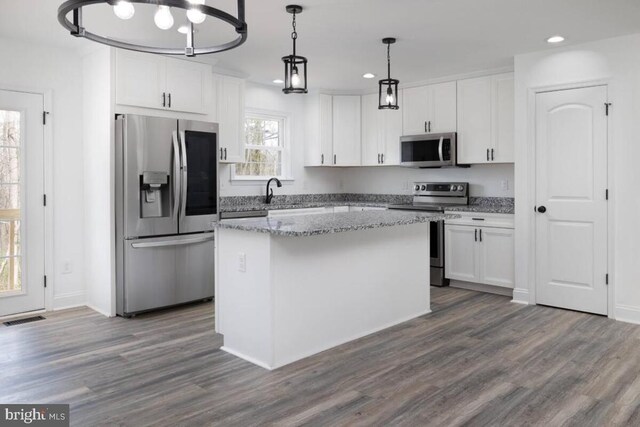 kitchen featuring stainless steel appliances, light stone countertops, white cabinets, a kitchen island, and decorative light fixtures