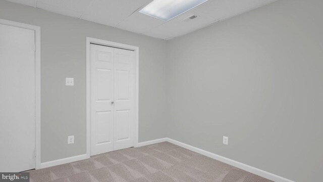 unfurnished bedroom with a paneled ceiling, light carpet, and a closet