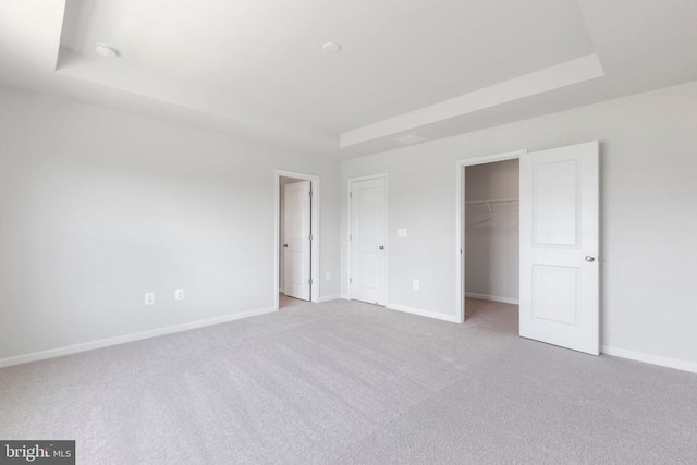 unfurnished bedroom with a raised ceiling, a walk in closet, light colored carpet, and a closet