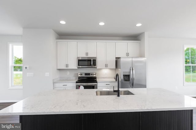 kitchen featuring appliances with stainless steel finishes, sink, white cabinets, a large island, and light stone counters