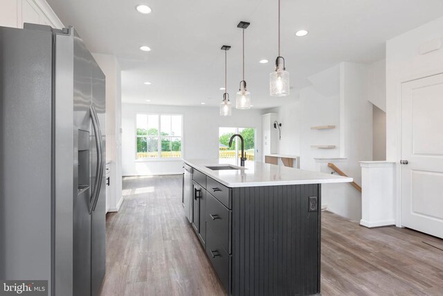 kitchen with sink, stainless steel refrigerator with ice dispenser, white cabinets, a center island with sink, and decorative light fixtures