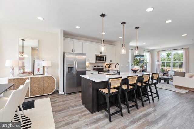 kitchen with sink, an island with sink, pendant lighting, stainless steel appliances, and white cabinets