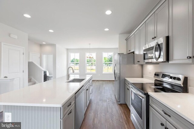 kitchen with gray cabinets, decorative light fixtures, an island with sink, sink, and stainless steel appliances