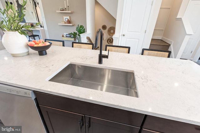 kitchen with light stone counters, sink, dark brown cabinets, and stainless steel dishwasher