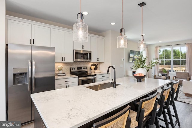 kitchen with a kitchen island with sink, sink, hanging light fixtures, and appliances with stainless steel finishes