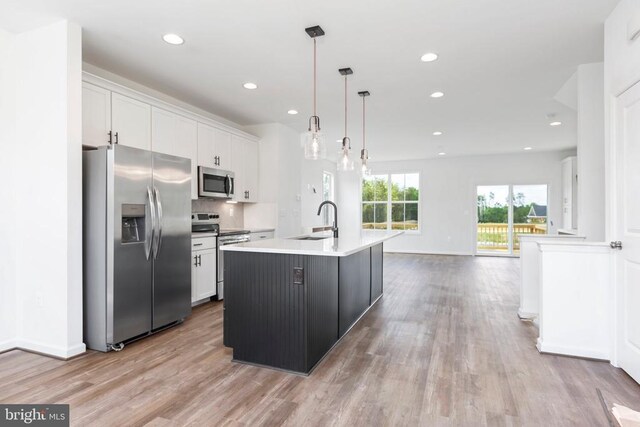 kitchen featuring sink, white cabinetry, decorative light fixtures, appliances with stainless steel finishes, and an island with sink