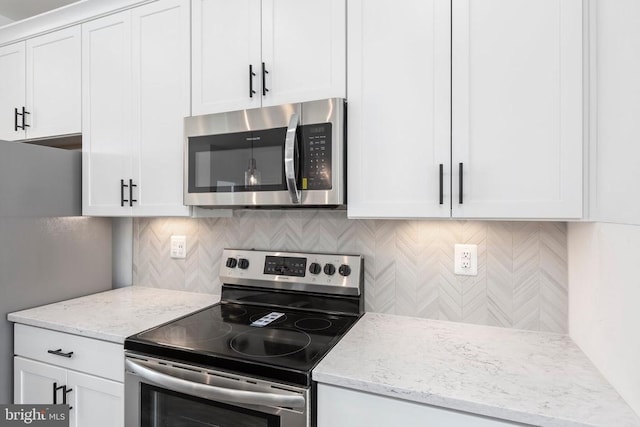 kitchen with stainless steel appliances, light stone counters, white cabinets, and backsplash