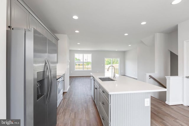 kitchen with sink, gray cabinetry, a center island with sink, stainless steel appliances, and light hardwood / wood-style floors