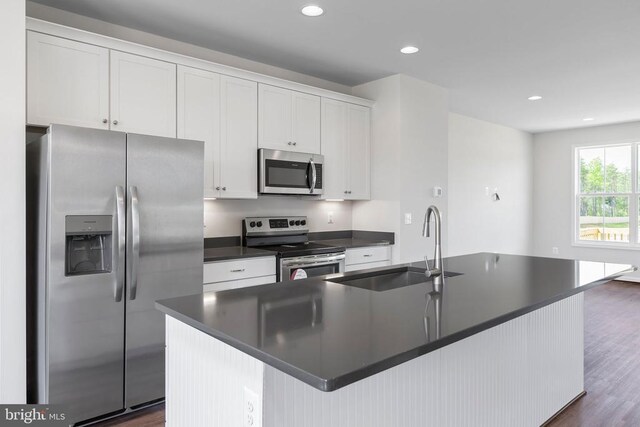 kitchen featuring stainless steel appliances, white cabinets, and a center island with sink