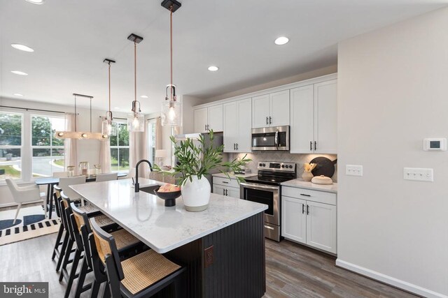 kitchen featuring a kitchen island with sink, hanging light fixtures, white cabinetry, and stainless steel appliances