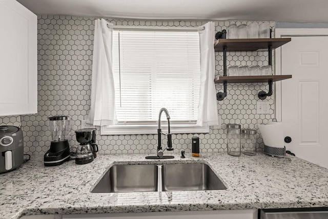 kitchen with white cabinetry, sink, light stone counters, and decorative backsplash