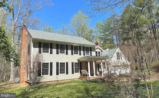 colonial home featuring a porch, a chimney, a shingled roof, and a front yard