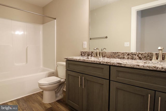 bathroom with double vanity, shower / bathing tub combination, wood finished floors, a sink, and toilet