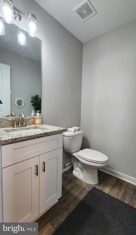half bathroom with visible vents, vanity, wood finished floors, toilet, and baseboards