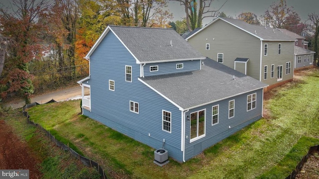 back of property featuring roof with shingles, a lawn, and central AC