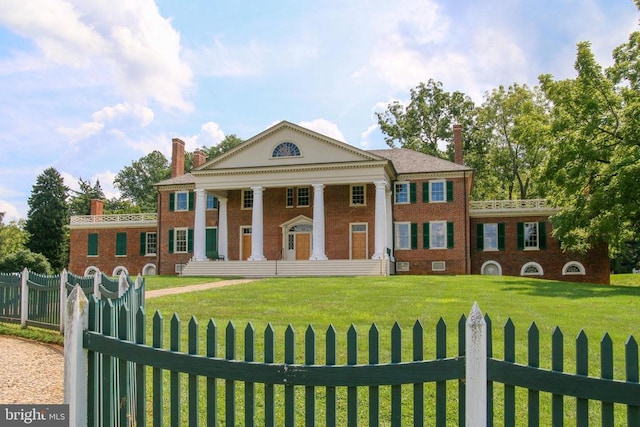 greek revival house featuring a fenced front yard, a front lawn, and brick siding