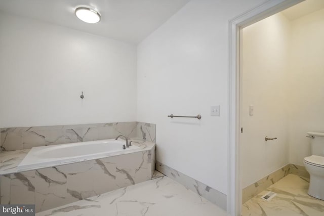 bathroom featuring tiled tub and toilet