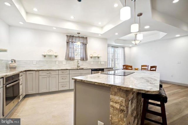 kitchen with appliances with stainless steel finishes, decorative light fixtures, a raised ceiling, and a breakfast bar area