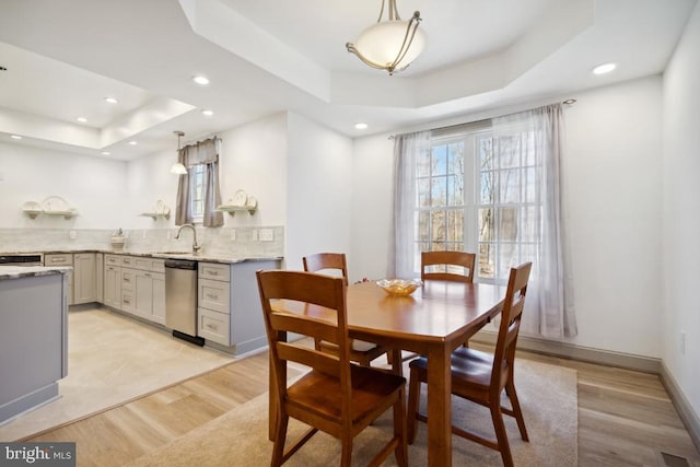 dining space featuring a raised ceiling, sink, and light hardwood / wood-style floors