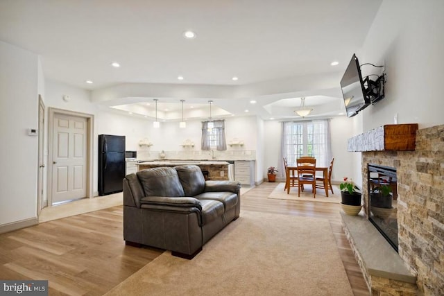 living room with light hardwood / wood-style flooring, a fireplace, and a tray ceiling