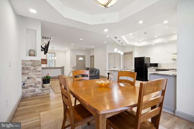 dining space with light hardwood / wood-style flooring and a raised ceiling