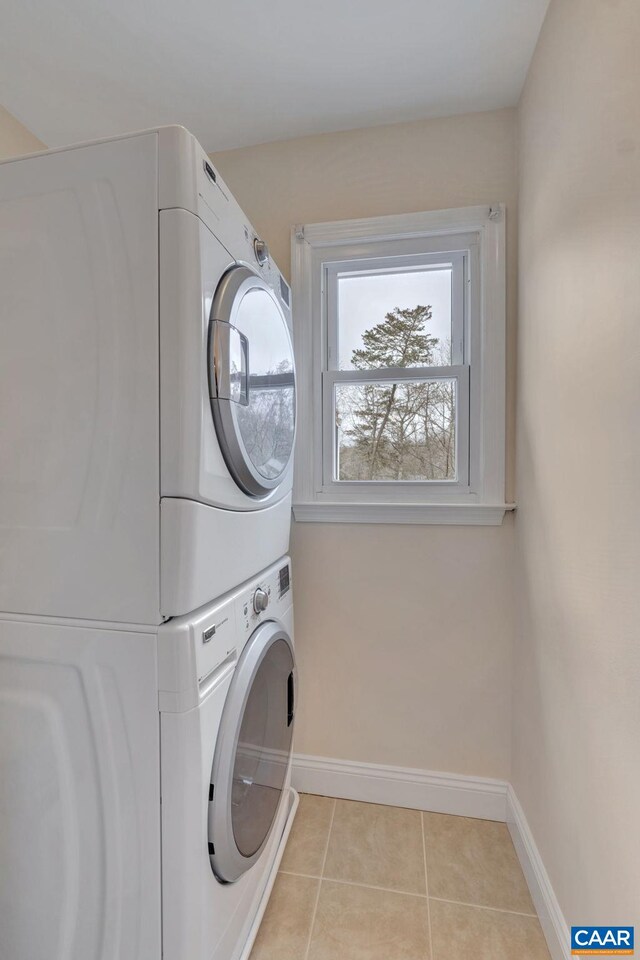 clothes washing area featuring light tile patterned floors, laundry area, stacked washer and clothes dryer, and baseboards