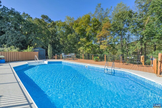 view of swimming pool with an outbuilding, fence, a fenced in pool, a storage unit, and a deck