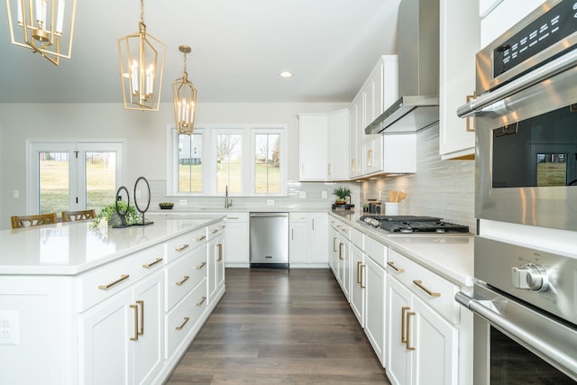 kitchen with appliances with stainless steel finishes, decorative light fixtures, white cabinets, a center island, and wall chimney range hood