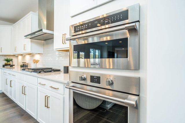 kitchen with wall chimney exhaust hood, white cabinetry, dark hardwood / wood-style floors, stainless steel appliances, and decorative backsplash