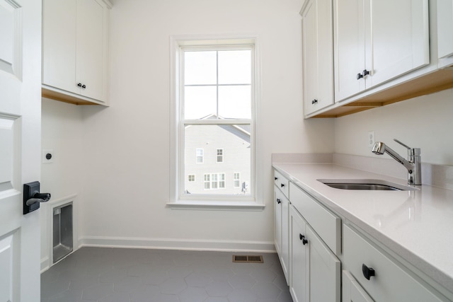 clothes washing area with cabinets, electric dryer hookup, sink, and dark tile patterned flooring