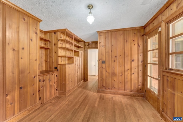 corridor featuring wood walls, a textured ceiling, and light wood-type flooring