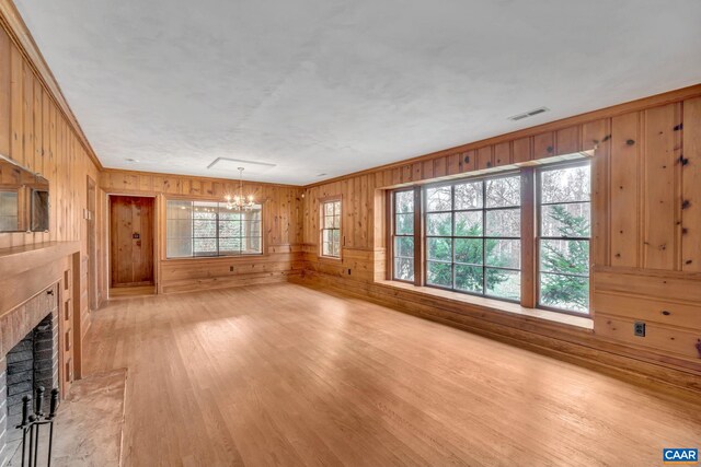 unfurnished living room featuring a notable chandelier, wood walls, a fireplace, and light hardwood / wood-style flooring