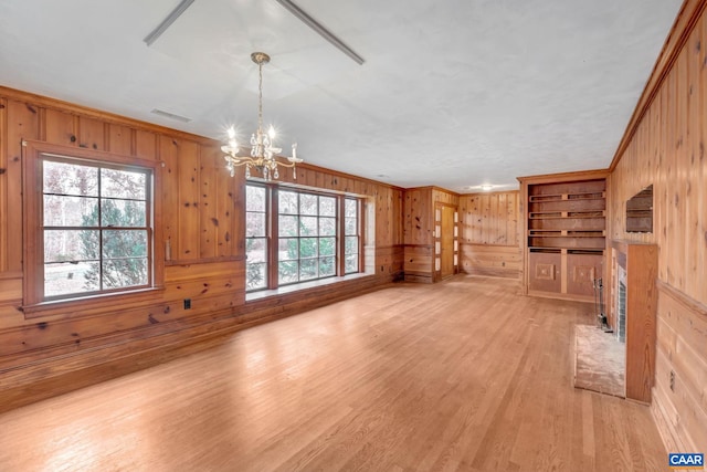 unfurnished living room featuring crown molding, a notable chandelier, wooden walls, and light hardwood / wood-style floors