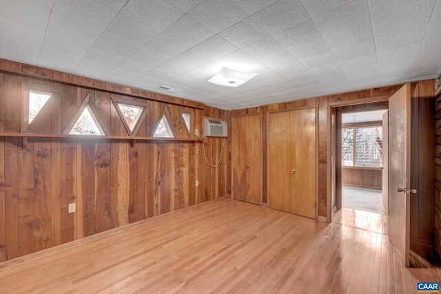 unfurnished room with a wall mounted air conditioner, light wood-type flooring, and wood walls