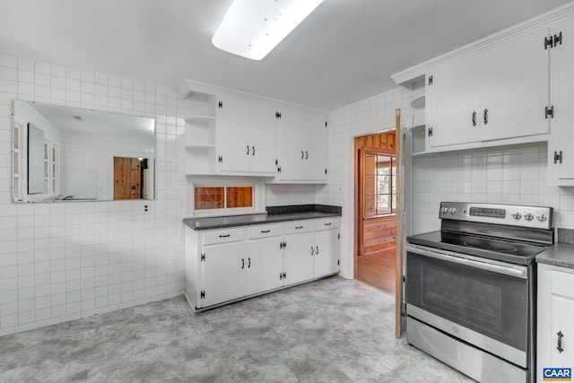 kitchen featuring stainless steel electric range, white cabinetry, backsplash, tile walls, and ornamental molding