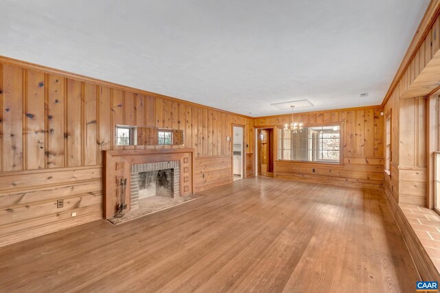 unfurnished living room featuring a brick fireplace, wooden walls, hardwood / wood-style floors, and an inviting chandelier