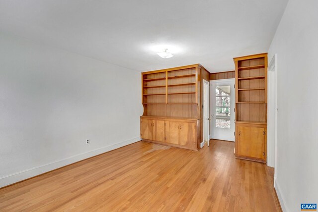 unfurnished living room featuring built in shelves and light wood-type flooring