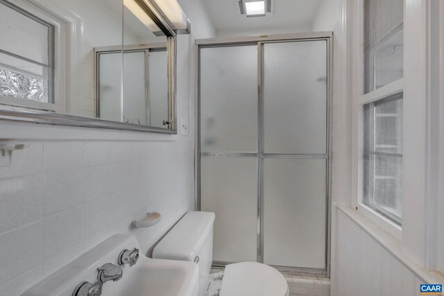 bathroom featuring walk in shower, toilet, sink, and tile walls