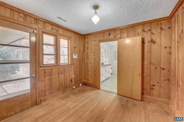 entrance foyer with crown molding, wood walls, a textured ceiling, and light wood-type flooring