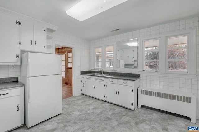 kitchen featuring white refrigerator, radiator heating unit, sink, and white cabinets