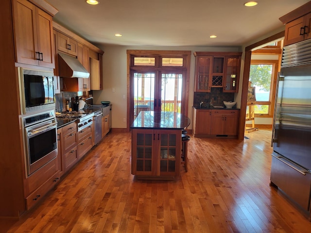 kitchen featuring backsplash, stainless steel appliances, ventilation hood, wood-type flooring, and french doors