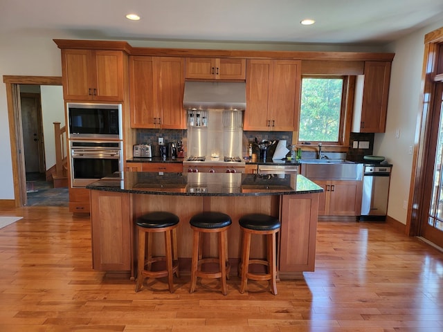 kitchen featuring black microwave, a center island, ventilation hood, dark stone counters, and stainless steel oven