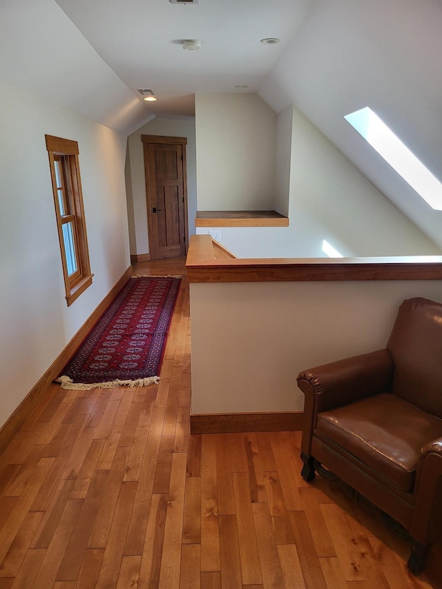 hallway featuring vaulted ceiling with skylight and light hardwood / wood-style flooring